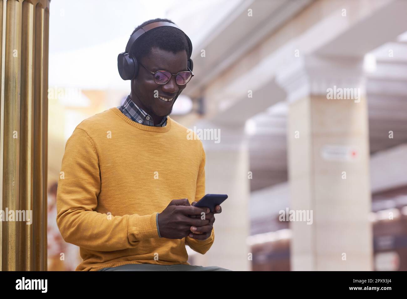 Ein lächelnder junger Mann mit kabellosen Kopfhörern kommuniziert online mit seinem Smartphone, während er in der U-Bahn steht Stockfoto
