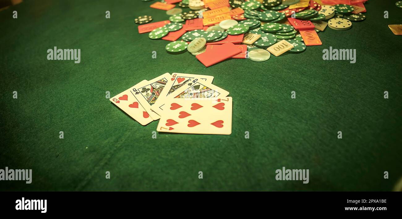 Eine chaotische Szene eines Pokerspiels mit Chips, die willkürlich über den Tisch verteilt sind. Verschwommener Hintergrund eines Pokerspielers, der am Tisch sitzt. Stockfoto