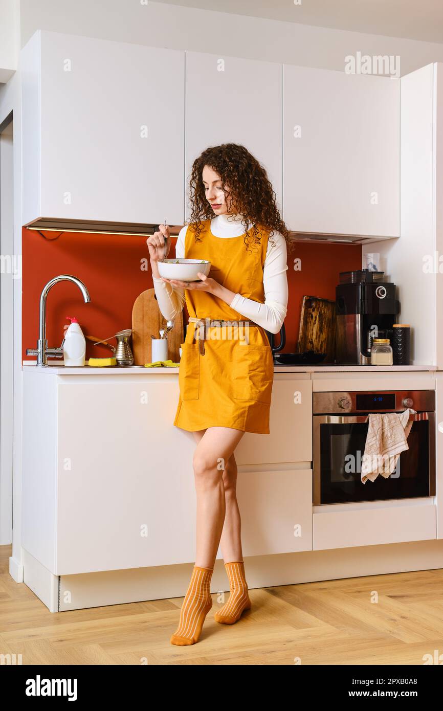 Schlanke Frau, die in Eile Salat isst, steht in der Küche Stockfoto