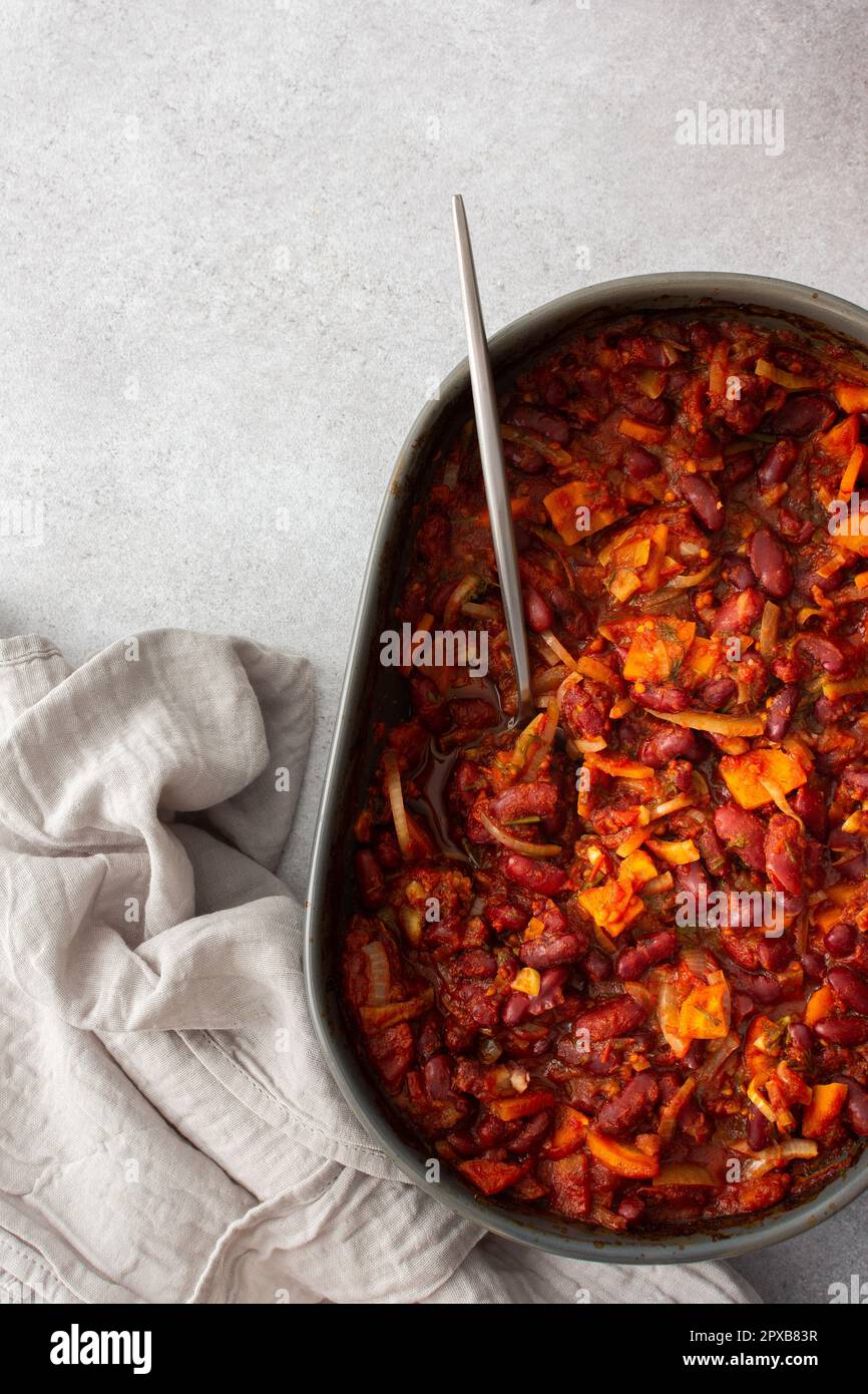 Gesundes Frühstück und Mittagessen, gedünstete rote Bohnen mit Karotten, Zwiebeln und Tomaten, Blick von oben auf eine ovale Keramikrösterei mit gedünsteten Hülsenfrüchten Stockfoto