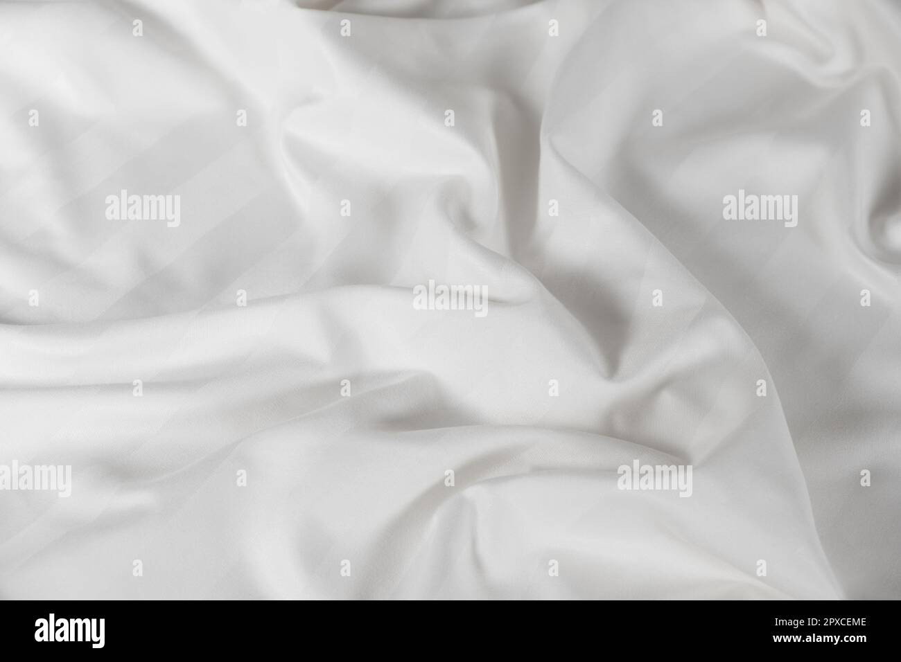 Satiniertes, weißes, zerknittertes Material, Draufsicht. Natürliche Bettwäsche, Laken, abstrakter Hintergrund aus luxuriösem Stoff, wellenförmige Falten Stockfoto