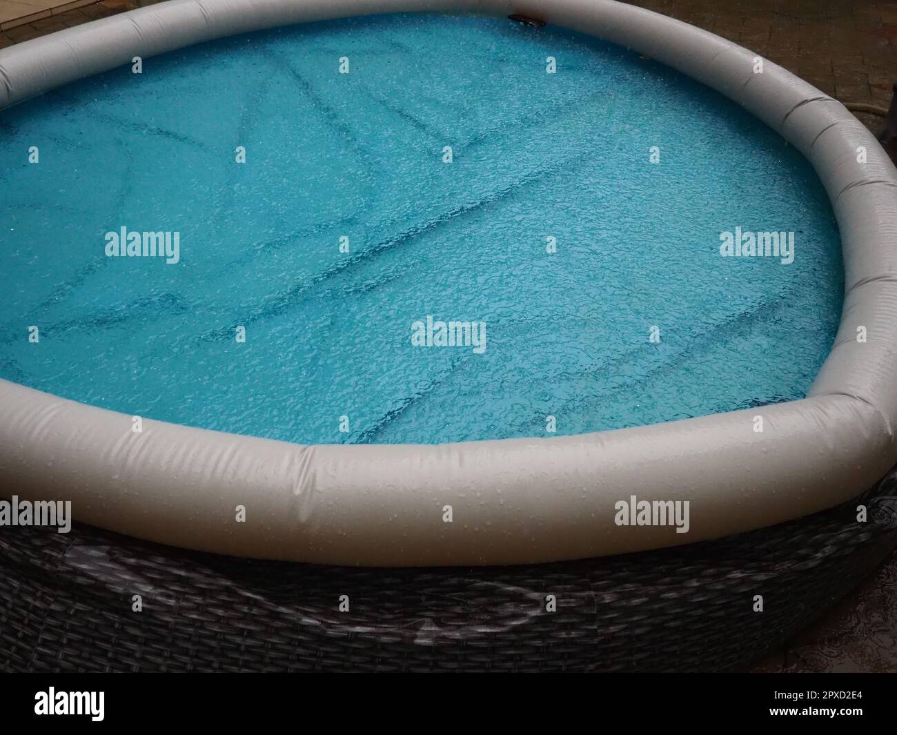Mit Wasser gefüllter Gummi-Rundpool. Blaues Wasser im Pool. Große Regentropfen fallen auf die Wasseroberfläche. Regnerisches Wetter im Hotel. Niemand Stockfoto