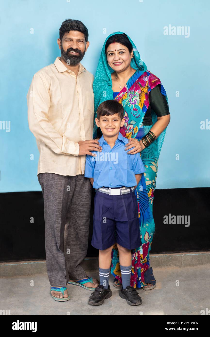 Junge, glückliche indische Eltern stehen mit dem kleinen Sohn in Schuluniform. Ländliches indien, Bildungskonzept. Stockfoto