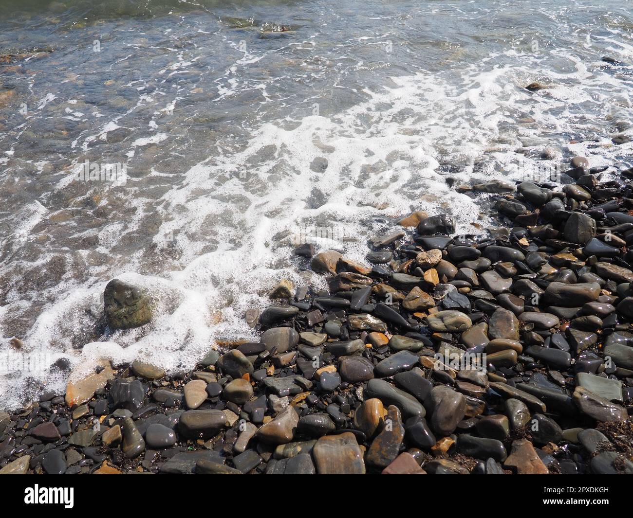 Felsiger Meeresstrand mit Wellen Sukko, Anapa, Krasnodar Territory, Russland. Meeresschaum auf Kieselsteinstrand von oben. Große abgerundete Kiesel und Felsbrocken i Stockfoto