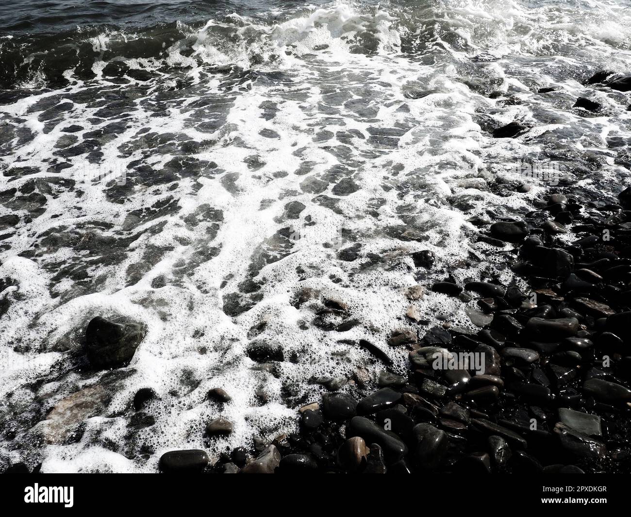 Felsiger Meeresstrand mit Wellen Sukko, Anapa, Krasnodar Territory, Russland. Meeresschaum auf Kieselsteinstrand von oben. Große abgerundete Kiesel und Felsbrocken i Stockfoto