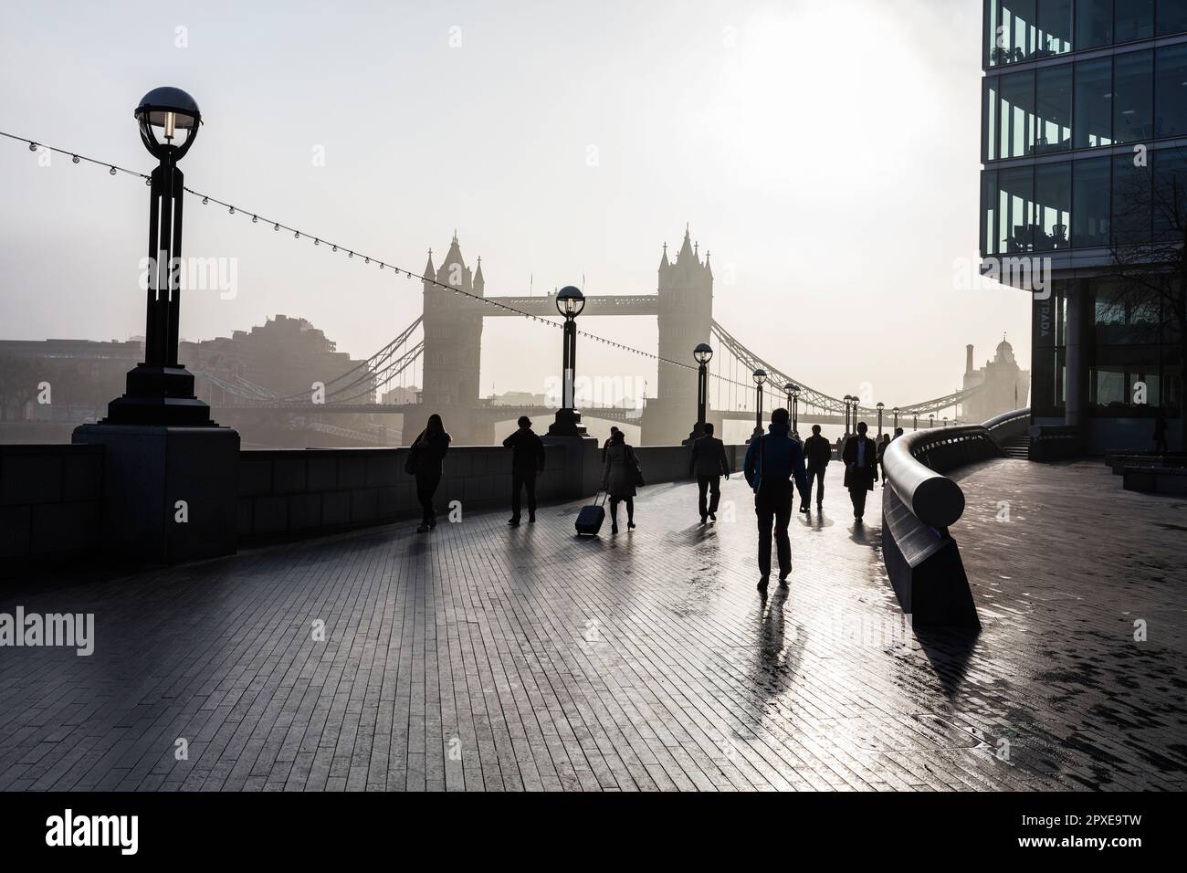 Die Leute, die am frühen Morgenaufgang zur Arbeit gehen, mit Nebel auf der Themse und Tower Bridge auf der South Bank Queens gehen am Rathaus vorbei, London. Stockfoto