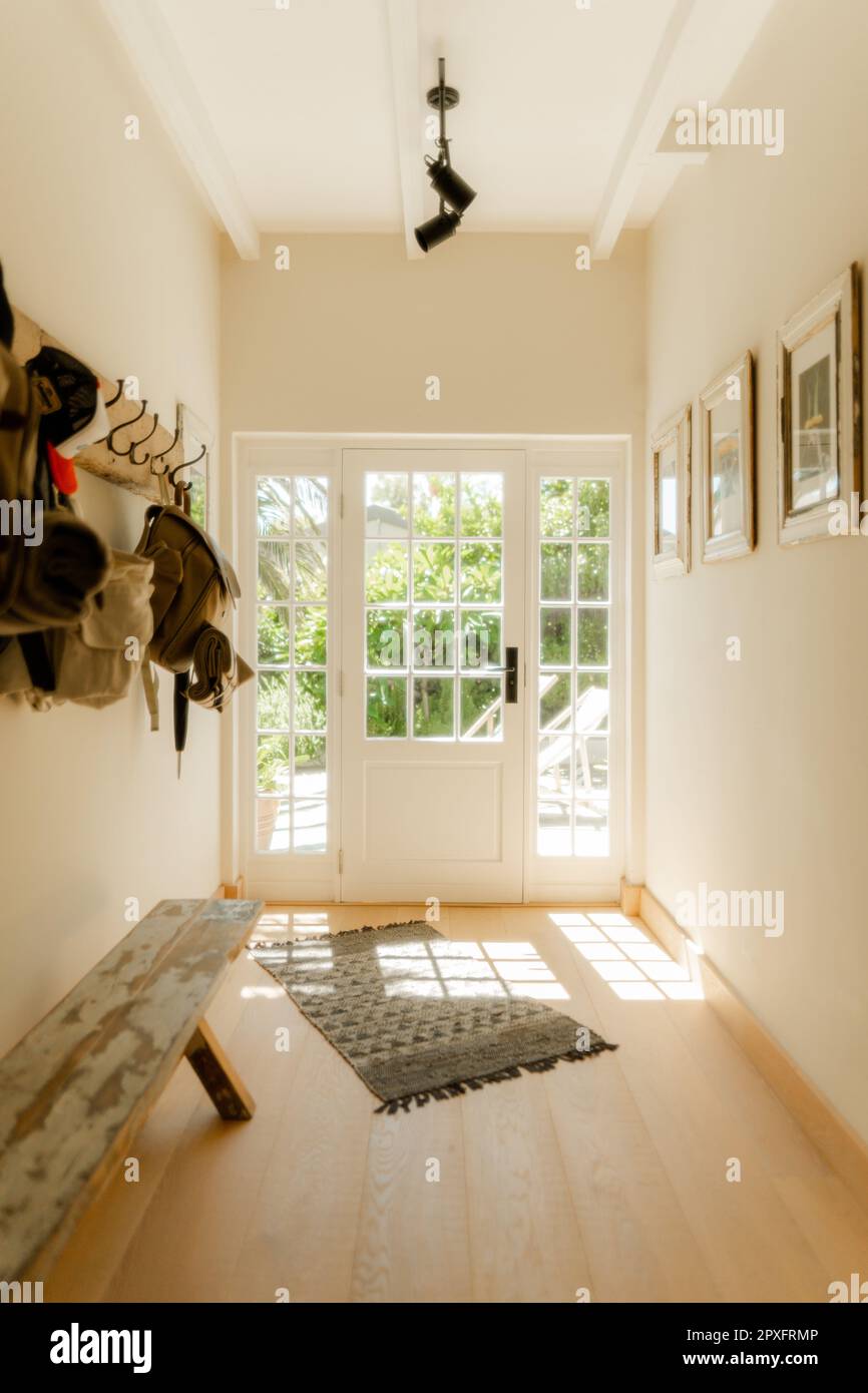 Ein hell beleuchteter Flur mit Kleiderständer und einer weißen Tür, die zum Garten führt Stockfoto