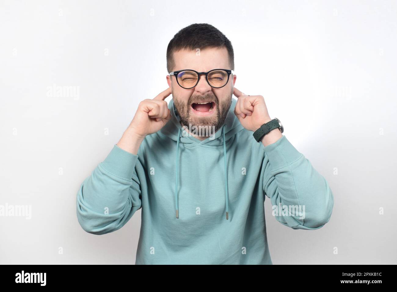 Ein junger Mann mit Brille hält sich die Ohren mit den Fingern zu und schreit Stockfoto