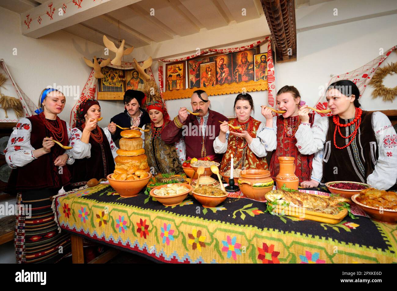 Familie in ukrainischen einheimischen Kostümen, die hinter dem Tisch mit traditionellen Gerichten zur Feier des Heiligabends versammelt sind. Ukrainische Volkstraditionen, Rekonstruktion Stockfoto