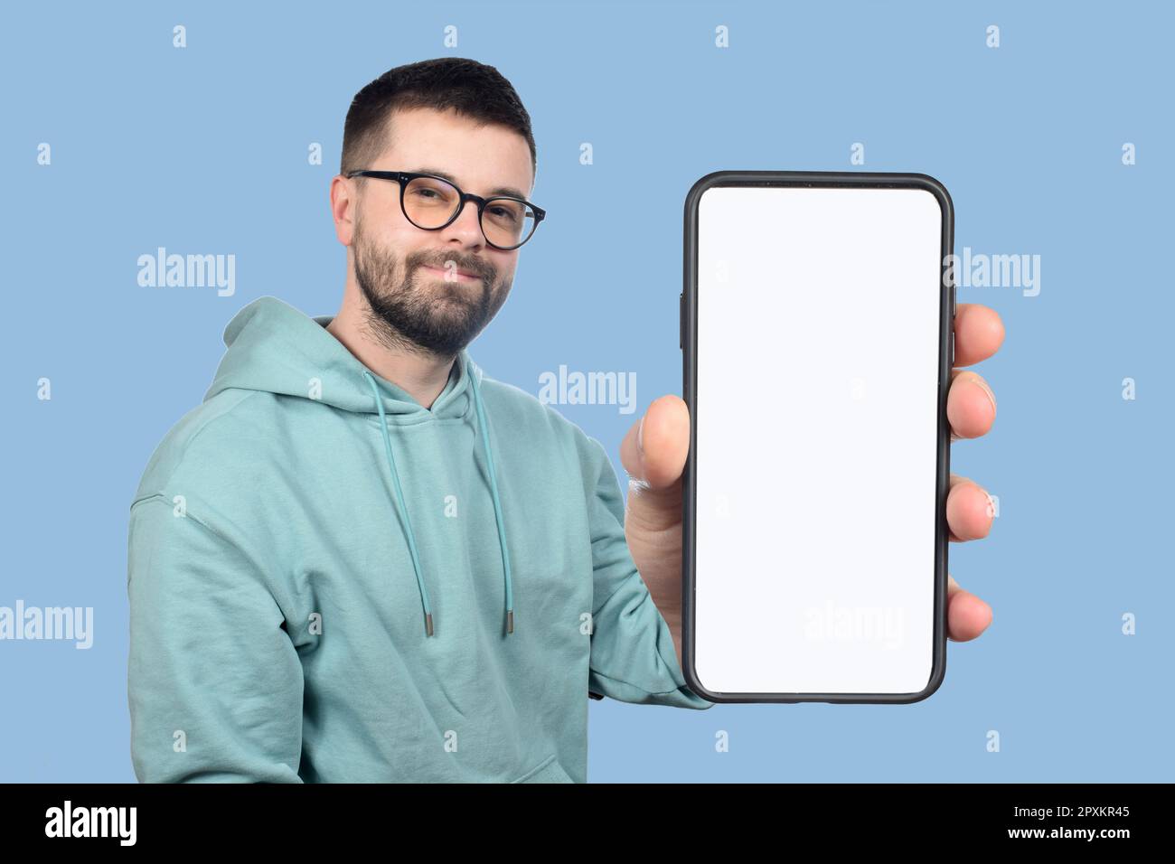 Ein junger Mann mit Brille und Bart zeigt ein Telefon mit einem leeren weißen Bildschirm Stockfoto