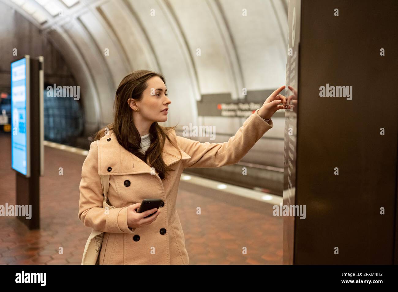 Eine junge Frau, die auf eine Landkarte schaut, um Wegbeschreibungen zu finden, und ein Handy in der Hand hält Stockfoto