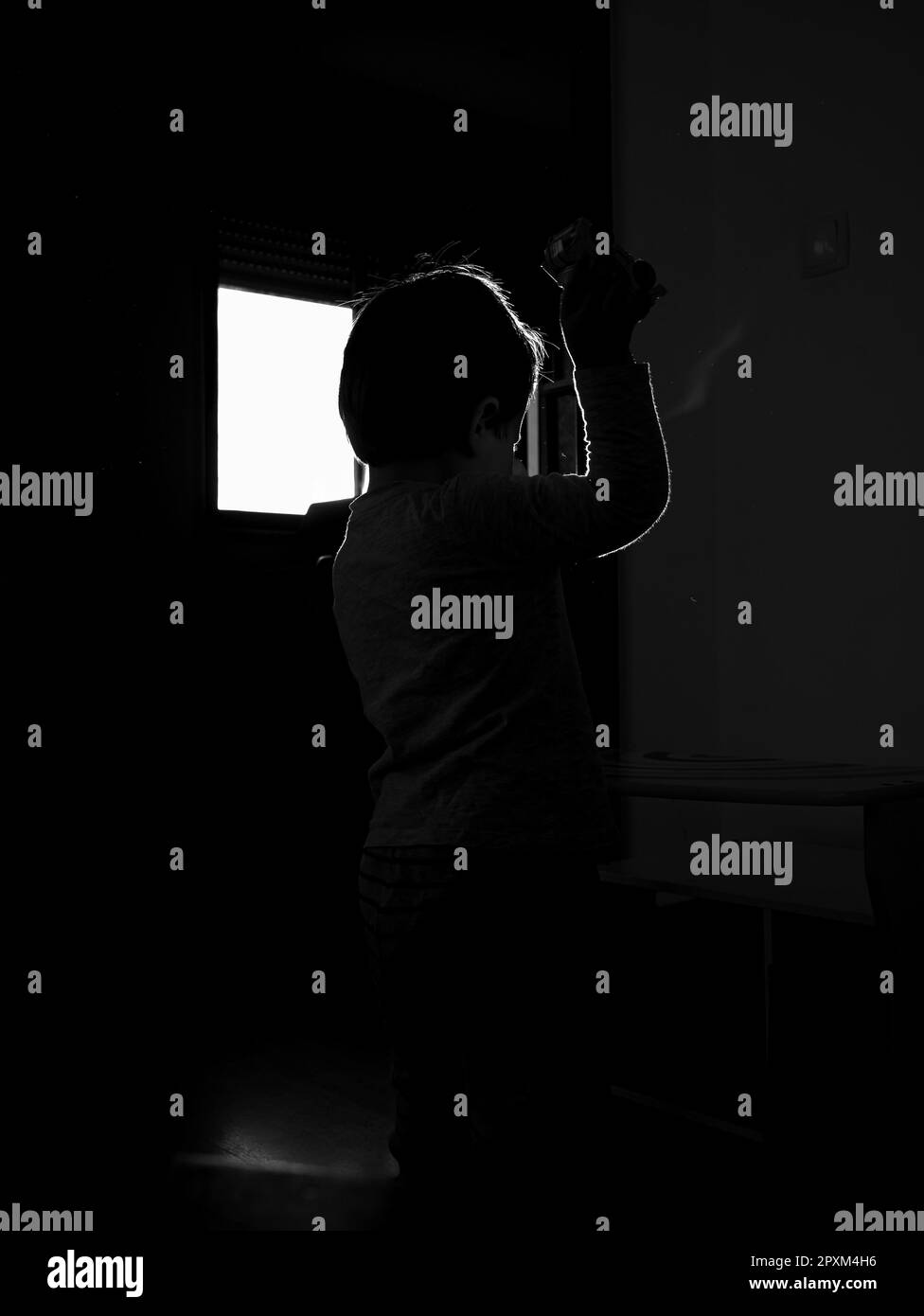 Ein Junge, der in einer dunklen Umgebung steht, während er eine Kamera in der Hand hält Stockfoto