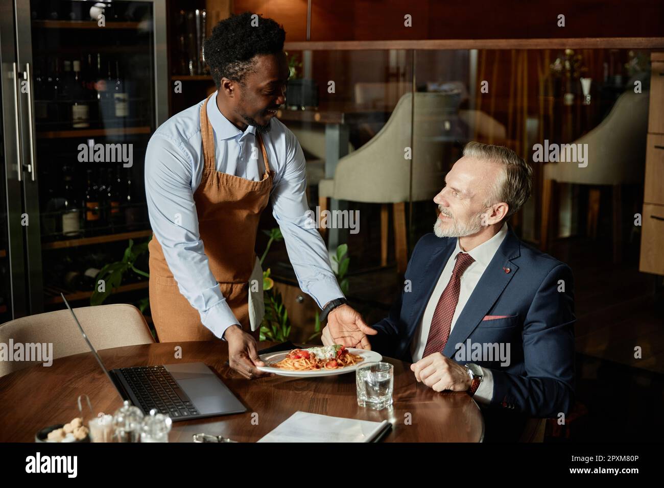 Ein afroamerikanischer Kellner serviert Geschäftsleuten mittags im Restaurant eine Mahlzeit Stockfoto
