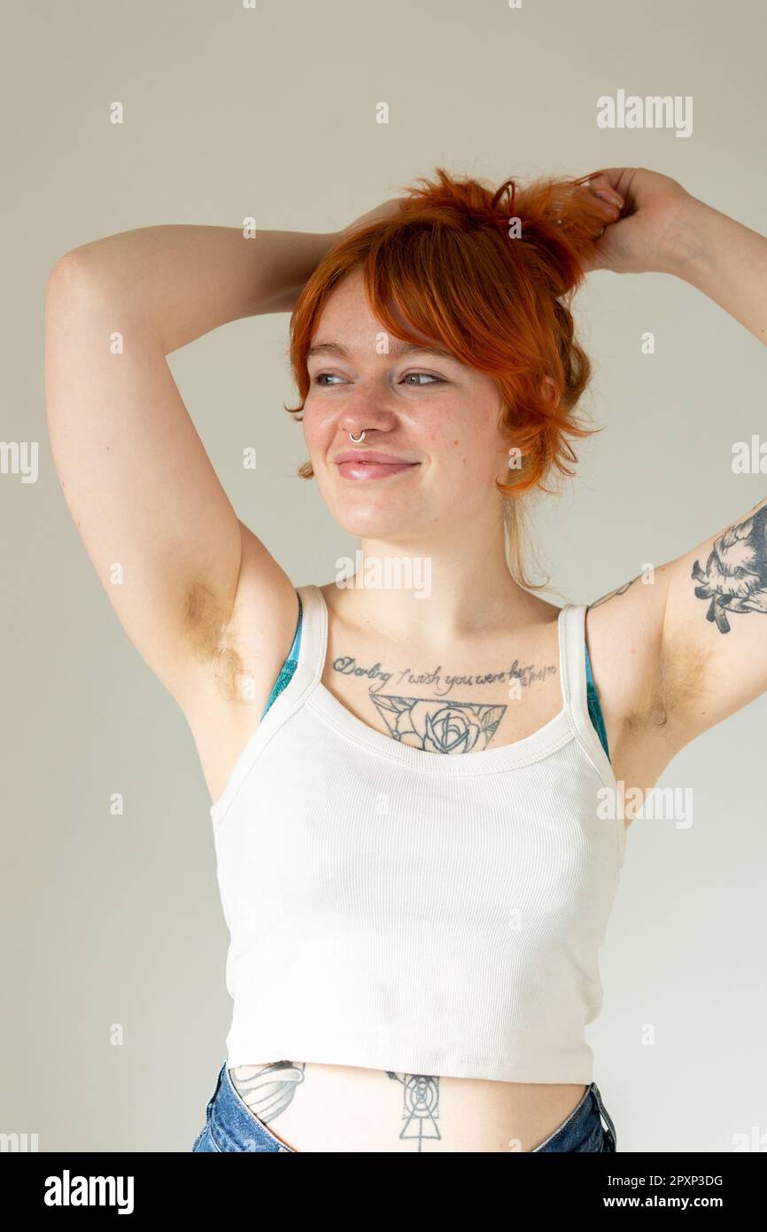 Eine schöne Frau Mitte zwanzig mit Tattoos und unrasierten Achselhöhlen, mit erhobenen Armen über dem Kopf Stockfoto