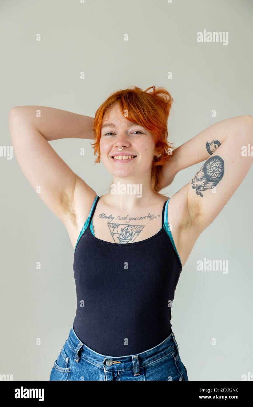 Eine schöne Frau Mitte zwanzig mit Tattoos und unrasierten Achselhöhlen, mit erhobenen Armen über dem Kopf Stockfoto