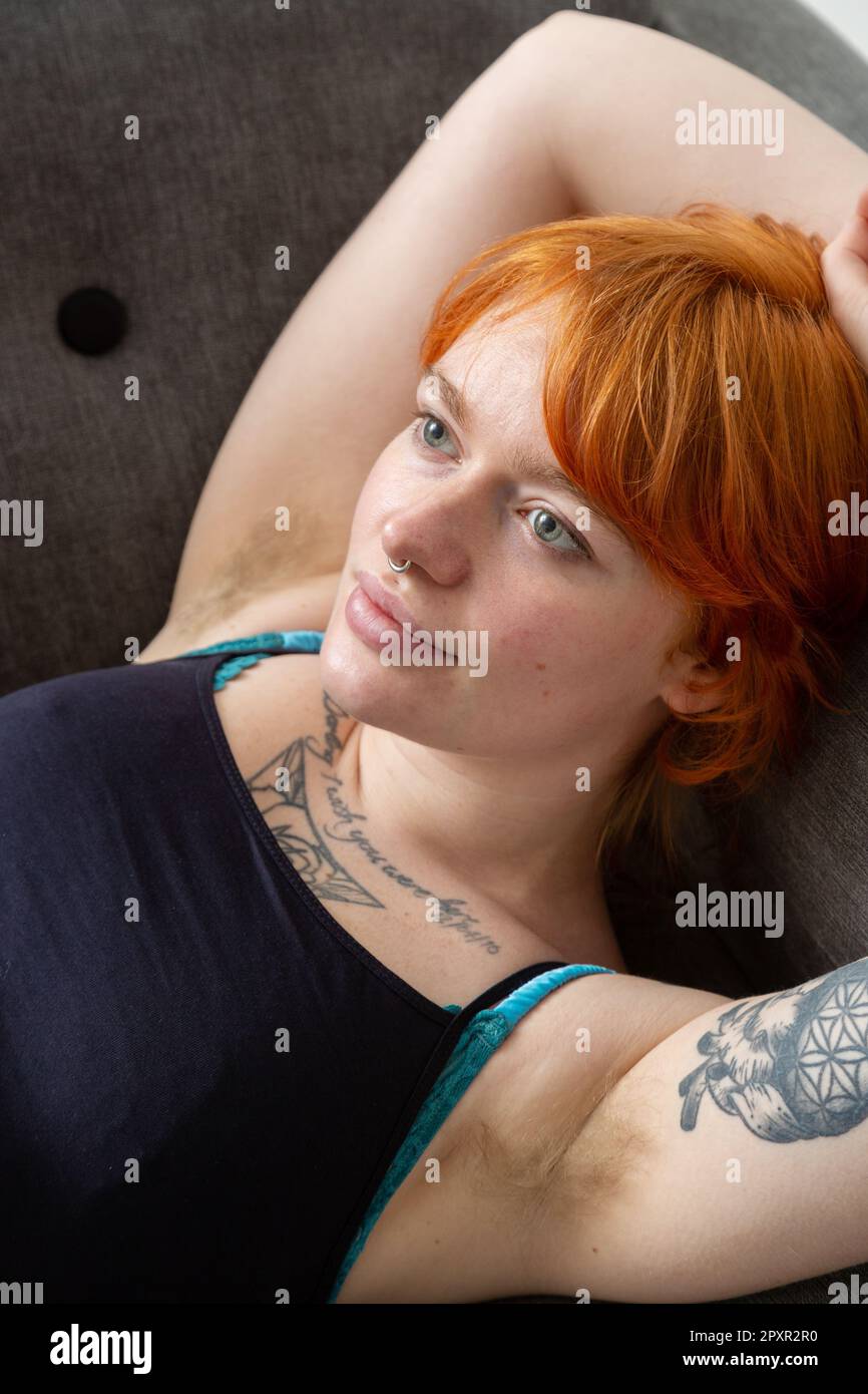Eine Frau mit behaarten Achselhöhlen, die auf einem Sofa liegt, mit den Armen über dem Kopf. Stockfoto