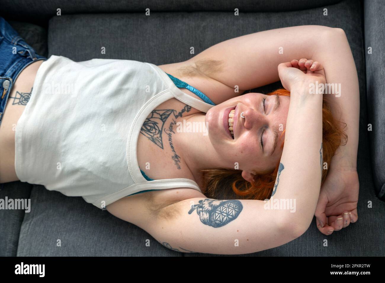 Eine Frau mit behaarten Achselhöhlen, die auf einem Sofa liegt, mit den Armen über dem Kopf. Stockfoto