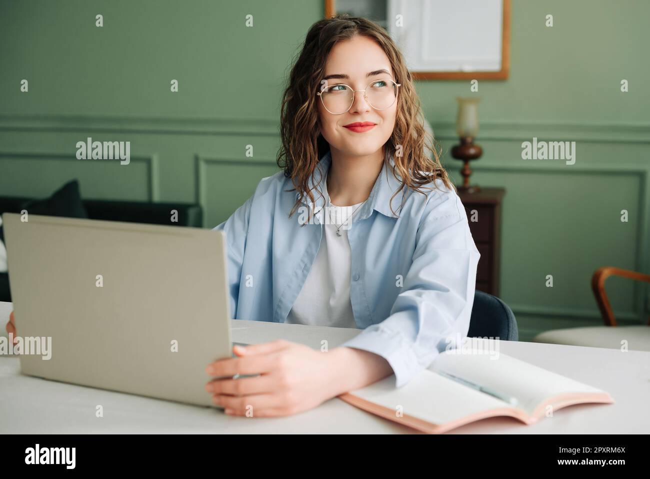 Lächelnde weibliche Mitarbeiterin, die in einem modernen Büro mit einem Notebook arbeitet, Marketingmanagerin oder Geschäftsfrau, die sich auf den Bildschirm konzentrierte, glücklich und selbstbewusst Stockfoto