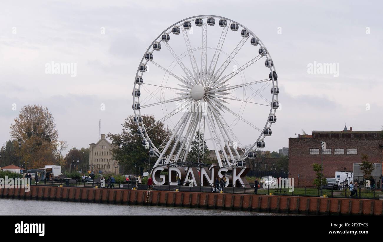 Die Leute gehen an Amber Sky Ferris Weel und dem Danziger Schild vorbei. Stockfoto