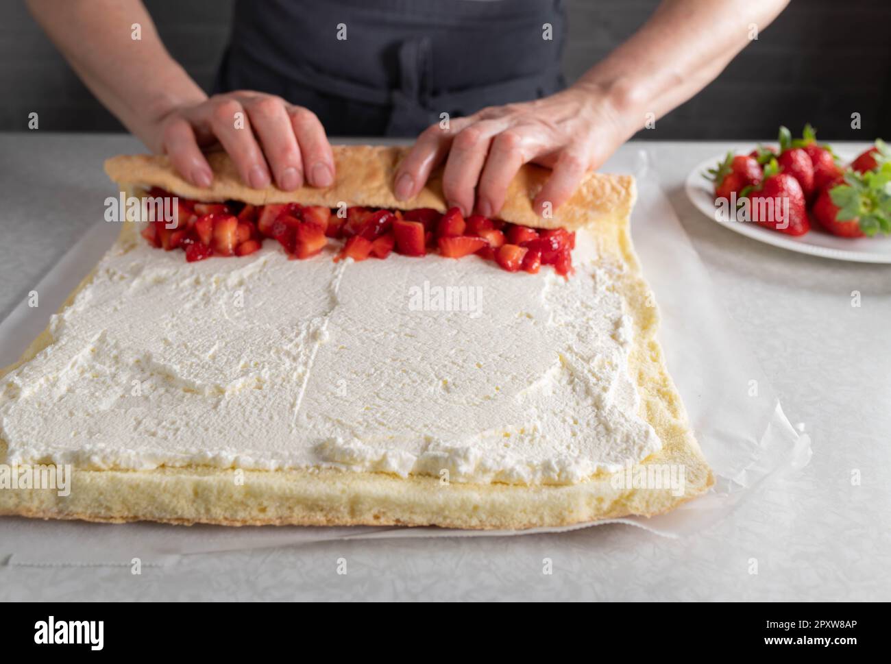 schweizer Brötchen. Mit Schlagsahne und Erdbeerfüllung von Frauenhänden auf dem Küchentisch zusammengerollt. Stockfoto