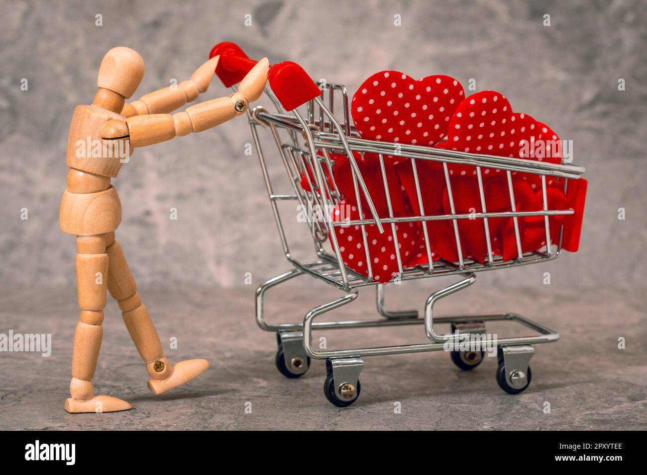 Schaufensterpuppe aus Holz, die einen Einkaufswagen voller Herzen zum Valentinstag schiebt Stockfoto