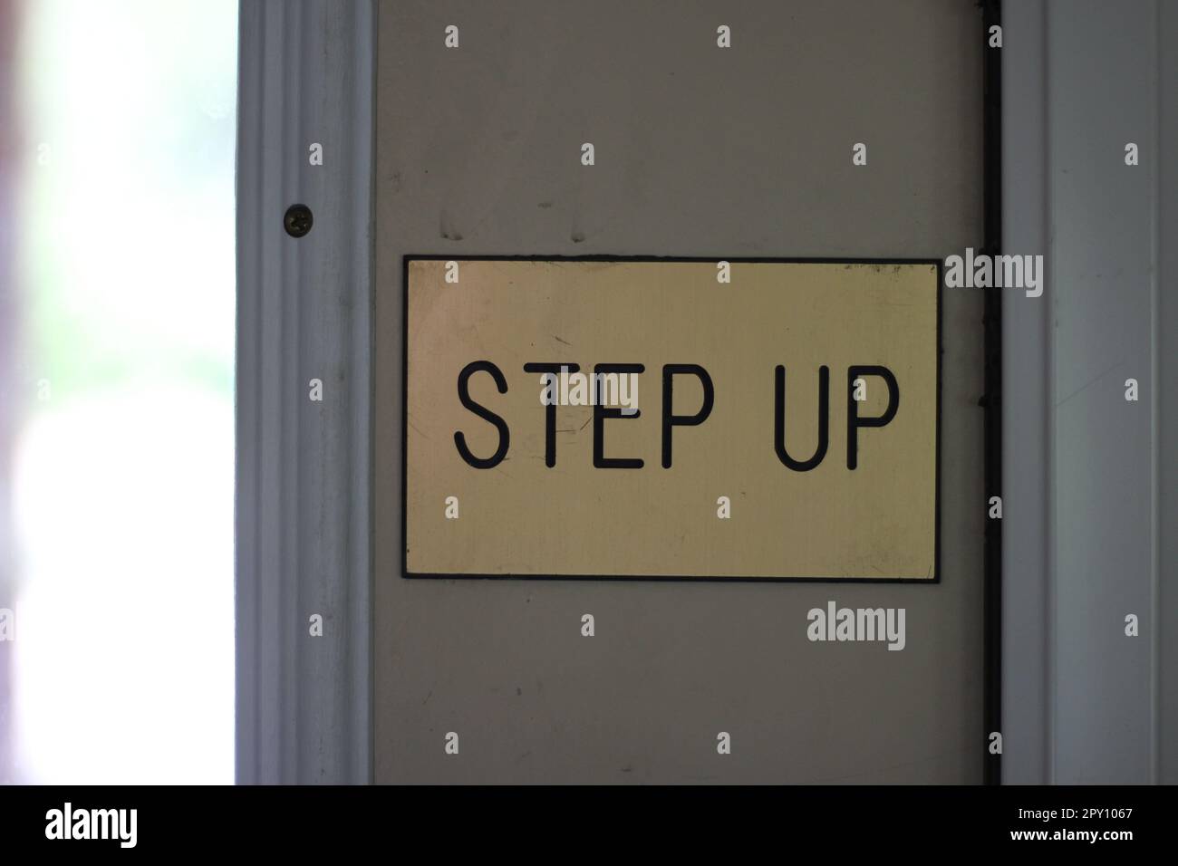 "STEPS UP" -Schild an der Tür eines Mietwohnungsbüros in den USA. Goldenes Schild mit schwarzer Schrift. Vorsicht, Stufe! Stockfoto