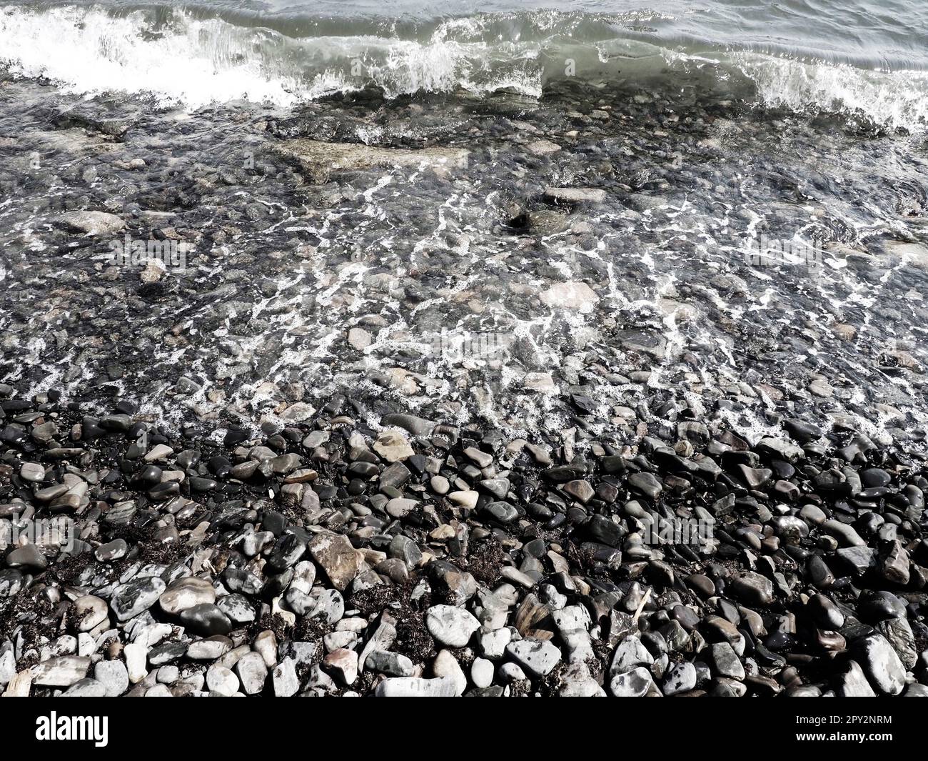 Felsiger Meeresstrand mit Wellen Sukko, Anapa, Krasnodar Territory, Russland. Meeresschaum auf Kieselsteinstrand von oben. Große abgerundete Kiesel und Felsbrocken i Stockfoto