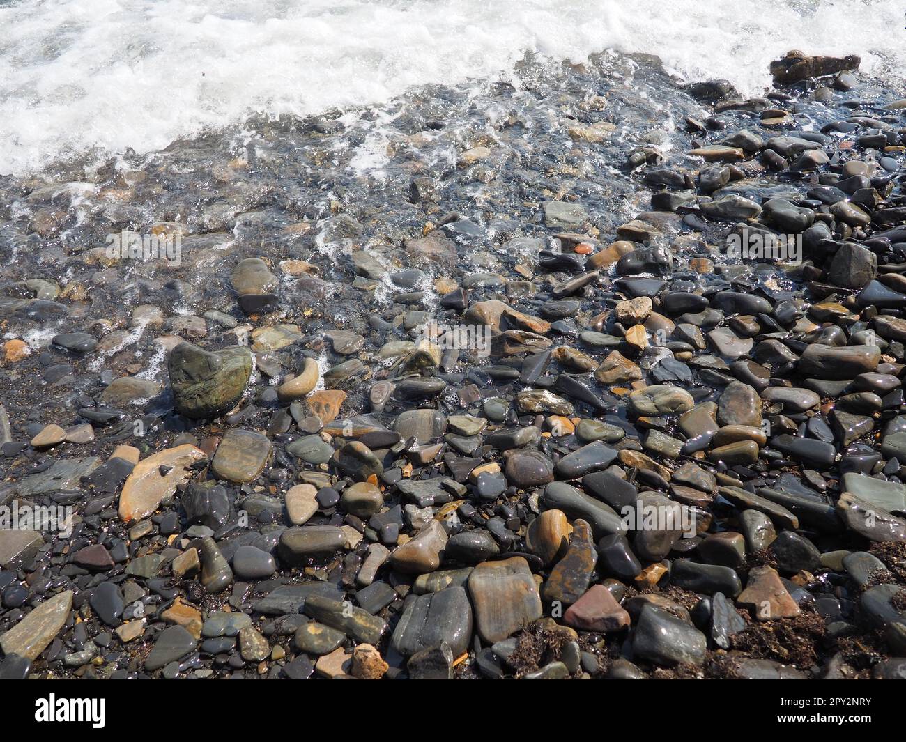 Felsiger Meeresstrand mit Wellen Sukko, Anapa, Krasnodar Territory, Russland. Meeresschaum auf Kieselsteinstrand von oben. Große abgerundete Kiesel und Felsbrocken i Stockfoto