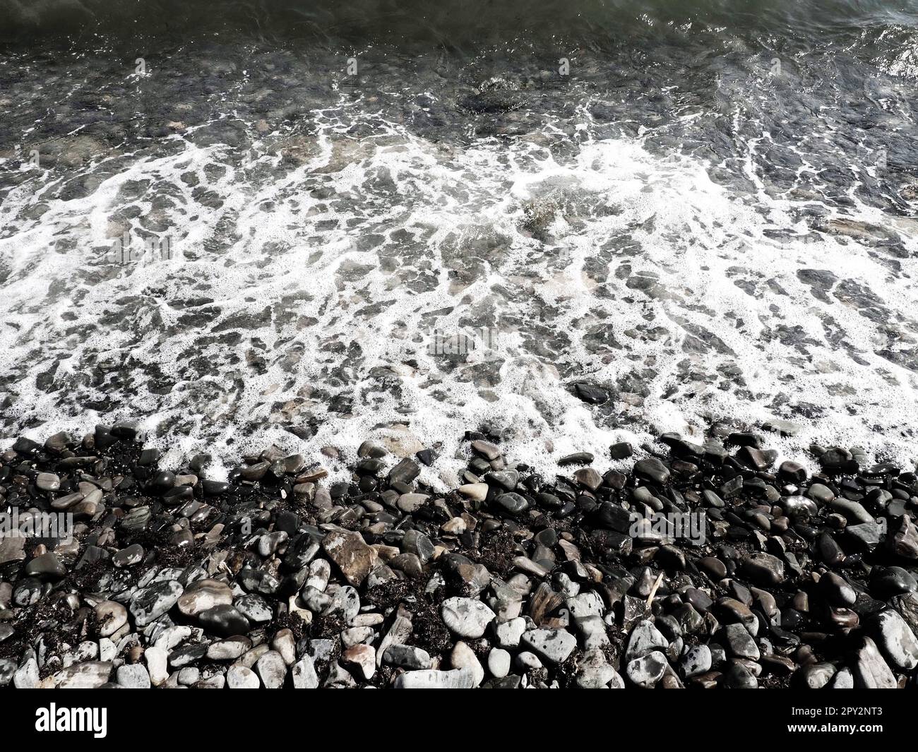 Felsiger Meeresstrand mit Wellen Sukko, Anapa, Krasnodar Territory, Russland. Meeresschaum auf Kieselsteinstrand von oben. Große abgerundete Kiesel und Felsbrocken i Stockfoto