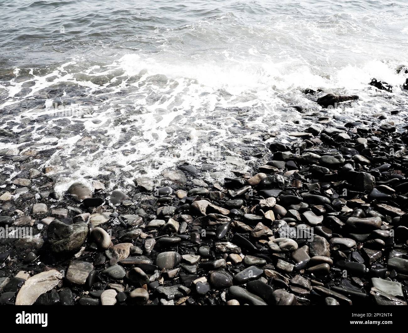 Felsiger Meeresstrand mit Wellen Sukko, Anapa, Krasnodar Territory, Russland. Meeresschaum auf Kieselsteinstrand von oben. Große abgerundete Kiesel und Felsbrocken i Stockfoto