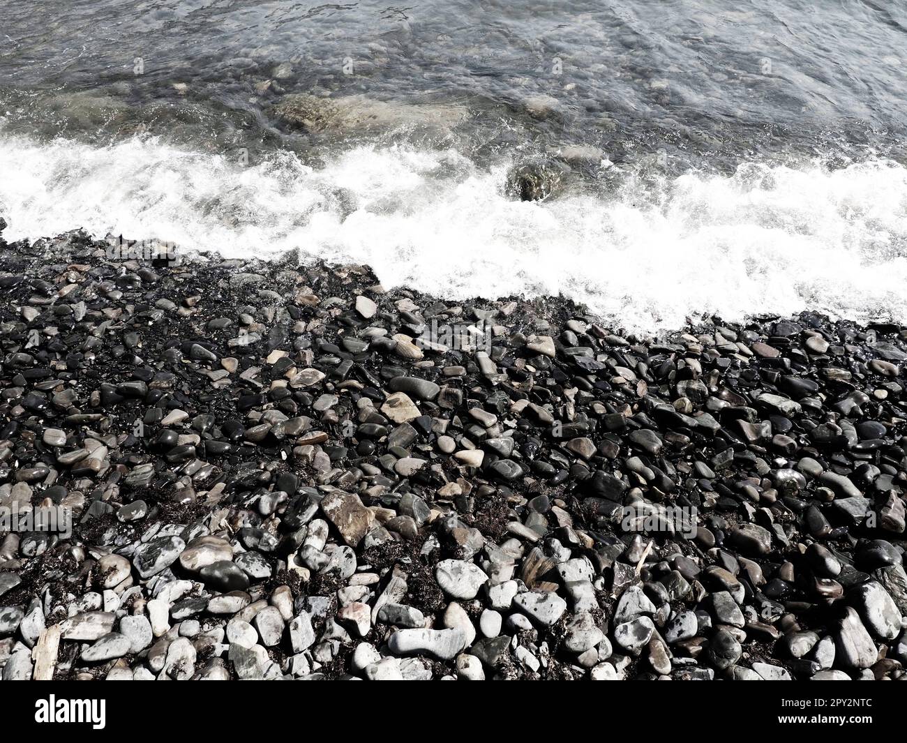 Felsiger Meeresstrand mit Wellen Sukko, Anapa, Krasnodar Territory, Russland. Meeresschaum auf Kieselsteinstrand von oben. Große abgerundete Kiesel und Felsbrocken i Stockfoto