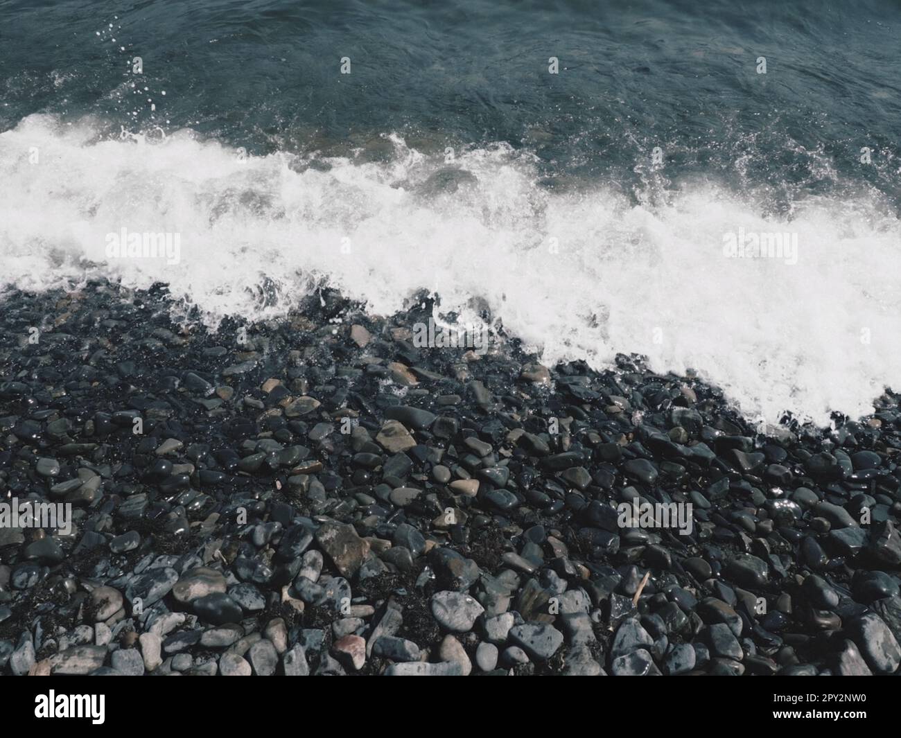 Felsiger Meeresstrand mit Wellen Sukko, Anapa, Krasnodar Territory, Russland. Meeresschaum auf Kieselsteinstrand von oben. Große abgerundete Kiesel und Felsbrocken i Stockfoto