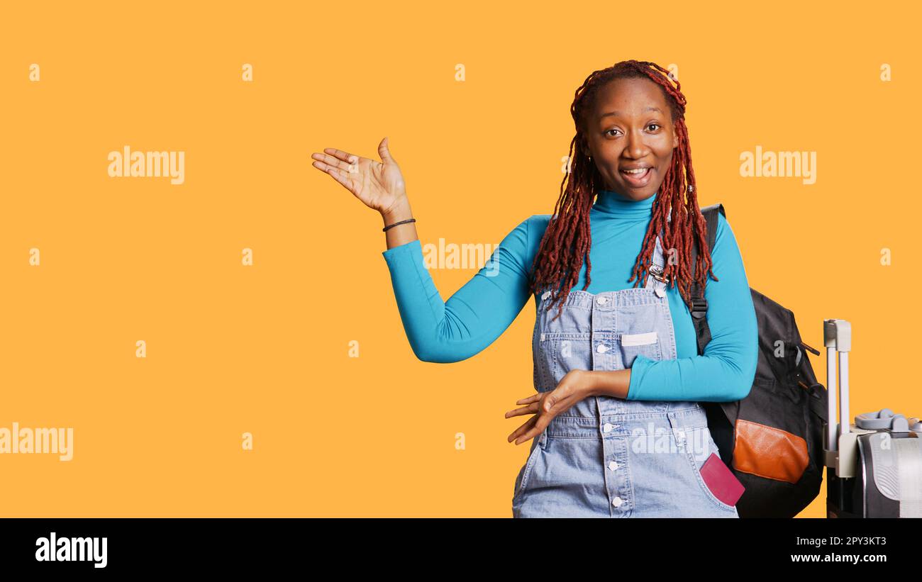 Glücklicher Erwachsener, der eine Präsentation im Studio hält und nach links oder rechts zeigt, um Werbung zu machen. Junge Frau, die mit Trolley und Koffer in die Stadt reist. Handgeführte Aufnahme. Stockfoto