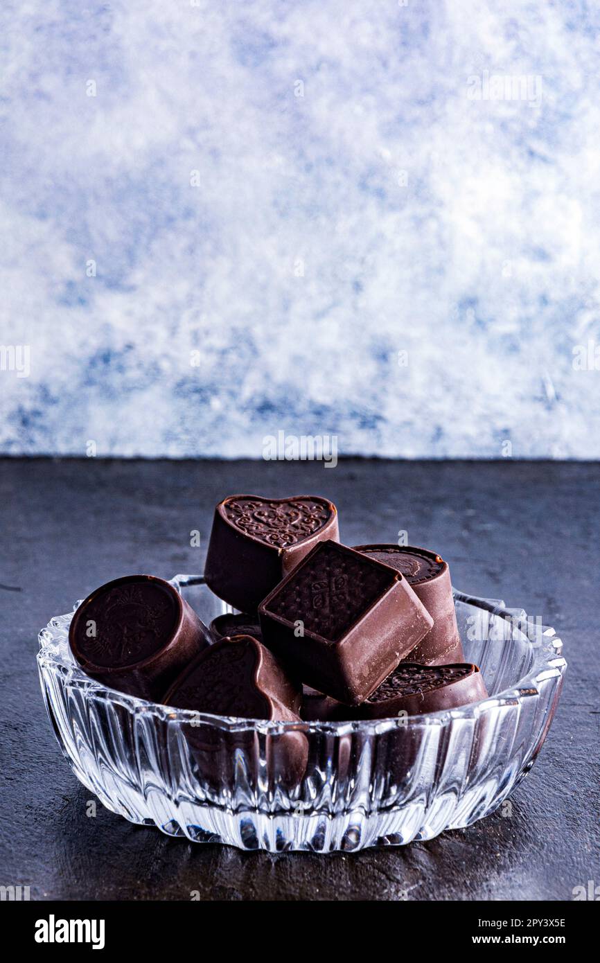 Pralinen auf einer Glasschale, fotografiert auf dunklem Hintergrund mit Kakaobohnen. Stockfoto