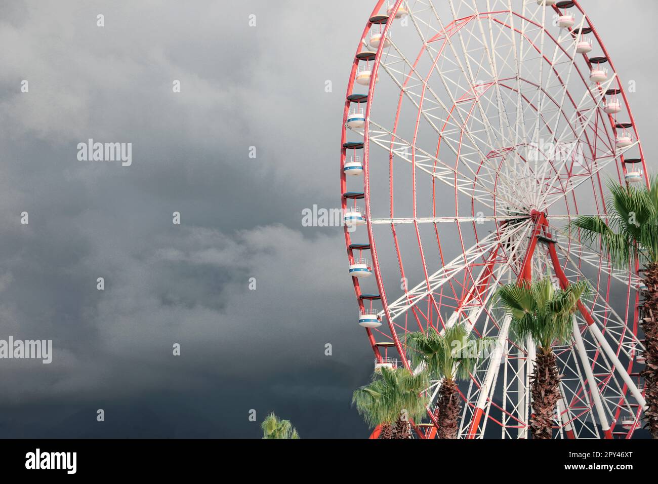 Wunderschönes großes Riesenrad und Palmen gegen den heftigen regnerischen Himmel im Freien. Platz für Text Stockfoto