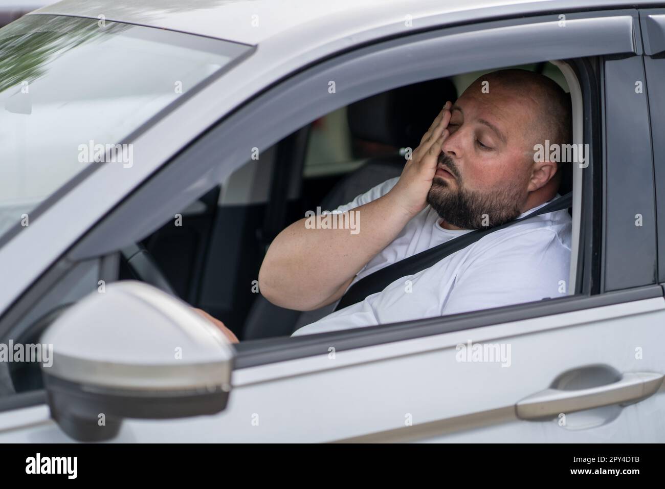 Ein müder, übergewichtiger Mann fährt bei heißem Sommerwetter ein Auto mit kaputter Klimaanlage. Stockfoto