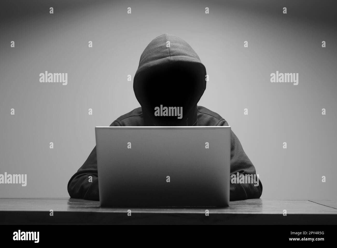 Mysteriöser Mann mit schwarzem Kapuzenpullover, der im dunklen Raum ein Notebook benutzt. Hacker- und Cybersicherheitskonzept. Stockfoto