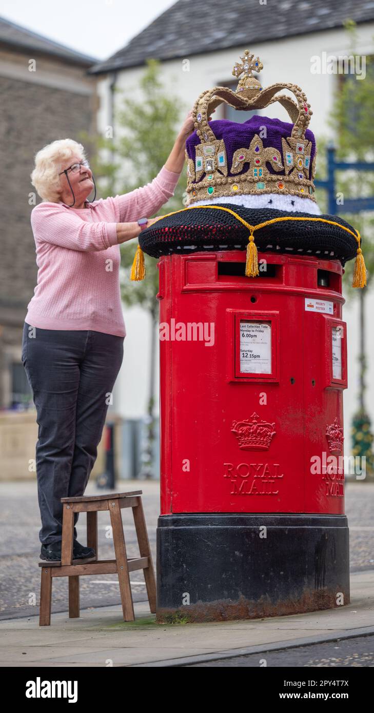 Selkirk, Großbritannien. 02. Mai 2023. 2. Mai 2023 das King-Charles-Krönungsfieber hat die schottische Grenzstadt Selkirk mit bunten gestrickten Hängekörben und einer wunderbaren riesigen Strickkrone oben auf dem roten Briefkasten der Stadt getroffen. Die Bombenangriffsgruppe von Souter Stormers ist für die bunten Szenen verantwortlich. Daphne Pratt, ein Team hinter dem extravaganten Strickstil, hat eine fantastische goldene Strickkrone geschaffen, die auf dem Hauptpostkasten der Stadt platziert wurde. Kredit: phil wilkinson/Alamy Live News Stockfoto