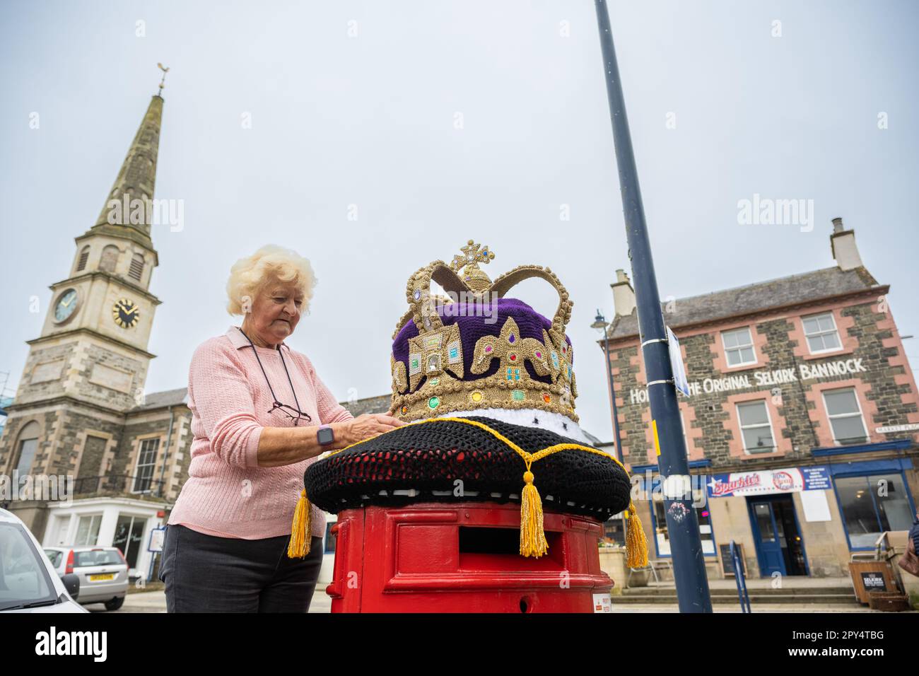 Selkirk, Großbritannien. 02. Mai 2023. 2. Mai 2023 das King-Charles-Krönungsfieber hat die schottische Grenzstadt Selkirk mit bunten gestrickten Hängekörben und einer wunderbaren riesigen Strickkrone oben auf dem roten Briefkasten der Stadt getroffen. Die Bombenangriffsgruppe von Souter Stormers ist für die bunten Szenen verantwortlich. Daphne Pratt, ein Team hinter dem extravaganten Strickstil, hat eine fantastische goldene Strickkrone geschaffen, die auf dem Hauptpostkasten der Stadt platziert wurde. Kredit: phil wilkinson/Alamy Live News Stockfoto