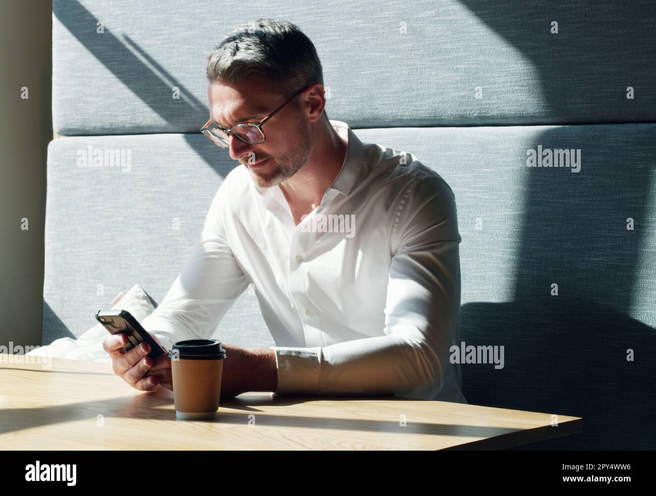 Kurze Pause, dann zurück zum Geschäft. Ein erwachsener Geschäftsmann, der ein Smartphone in einem modernen Büro verwendet. Stockfoto