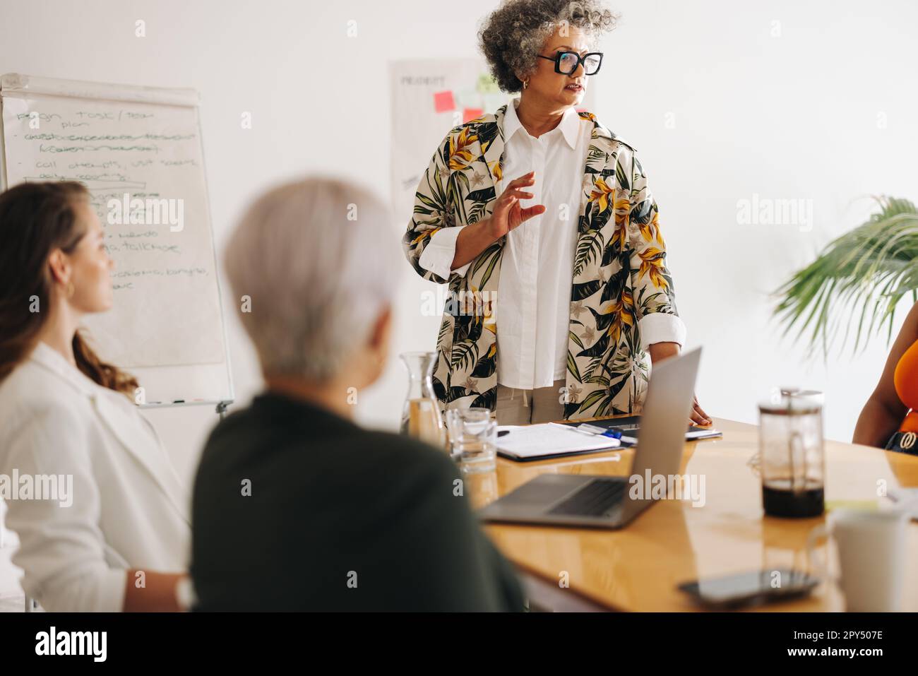 Die Geschäftsleiterin führt während eines Meetings ein Gespräch mit ihren Kollegen. Reife Geschäftsfrau teilt ihre Ideen mit ihrem Team. Multikulturelle Geschäfte Stockfoto