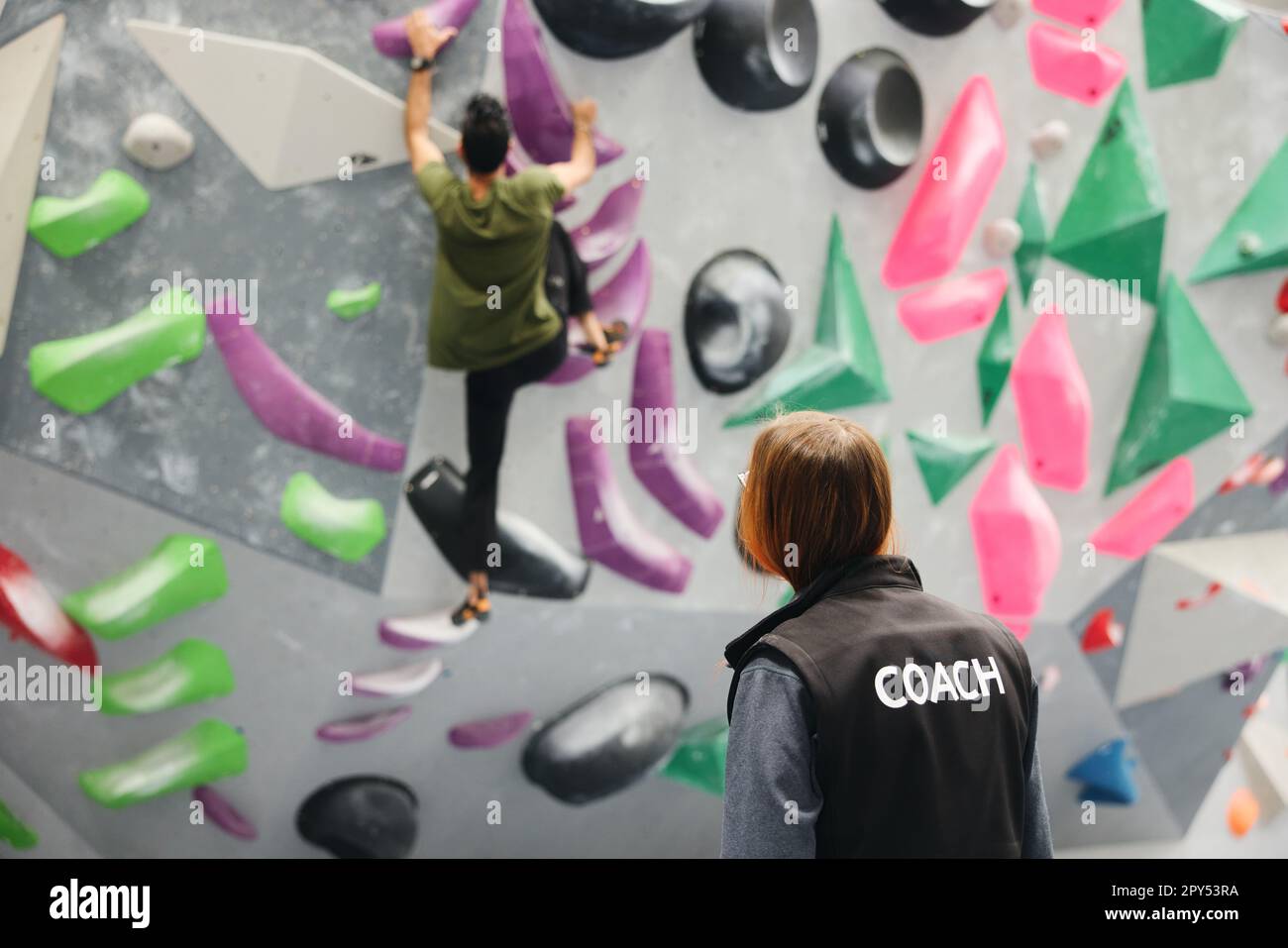 Eine Kutscherin beobachtet den Mann beim Klettern an die Wand im Hallenarbeitsplatz Stockfoto