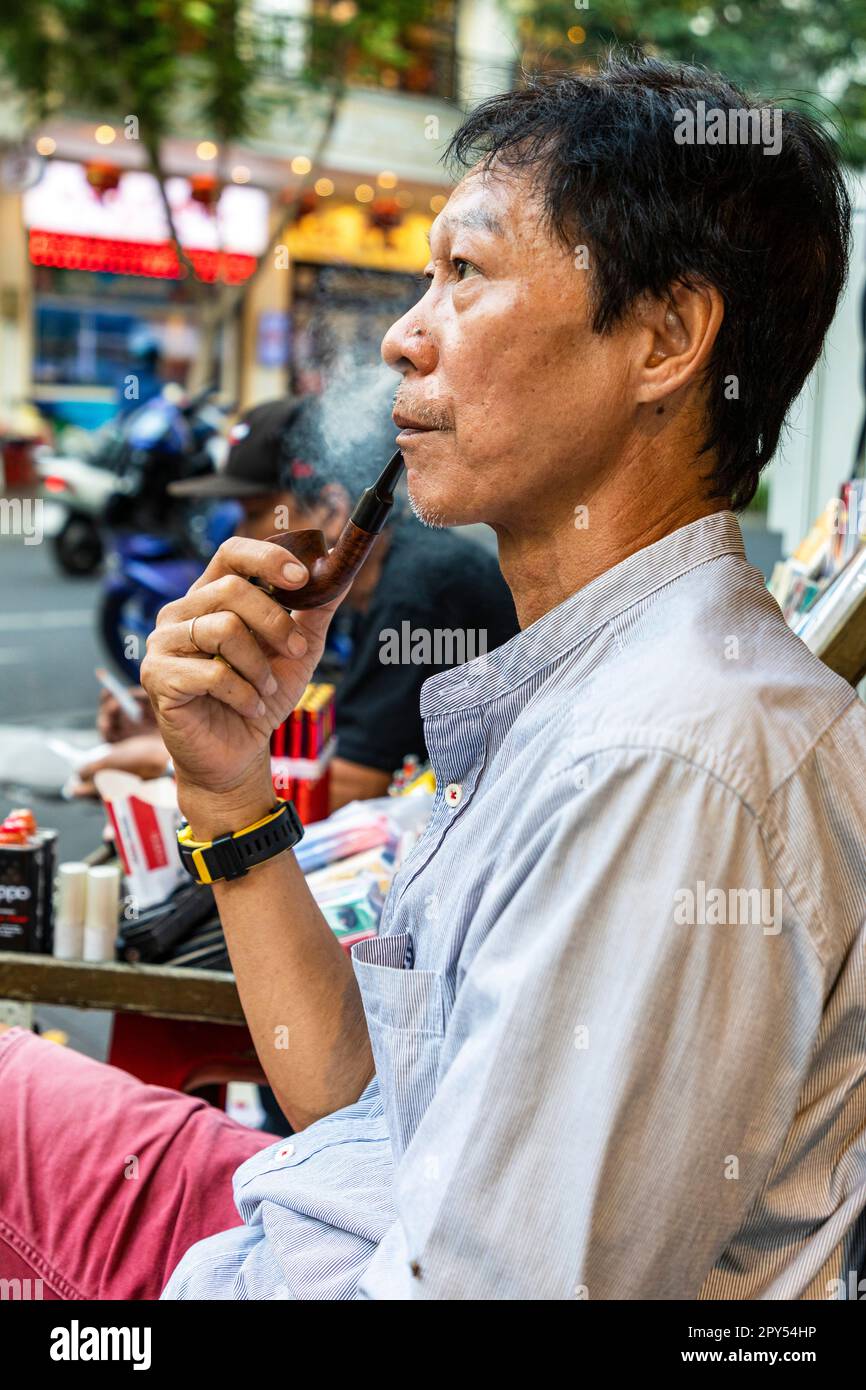 Ein vietnamesischer Mann, der Pfeife raucht, sitzt im Straßencafé, Ho Chi Minh City, Vietnam Stockfoto