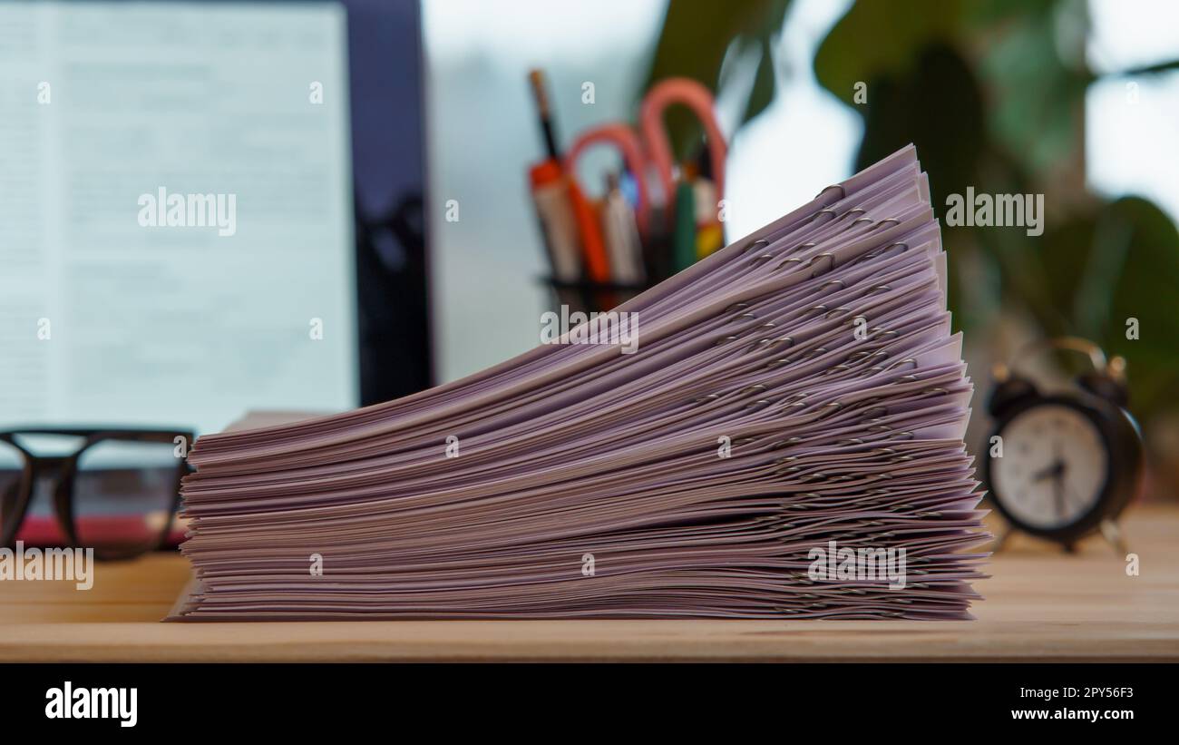 Zusammenstellung eines Stapels von Papieren, sortiert mit Büroklammern, Gläsern, Uhr, Büromaterial in der Nähe des Laptops auf dem Schreibtisch. Arbeitsbereich. Stockfoto