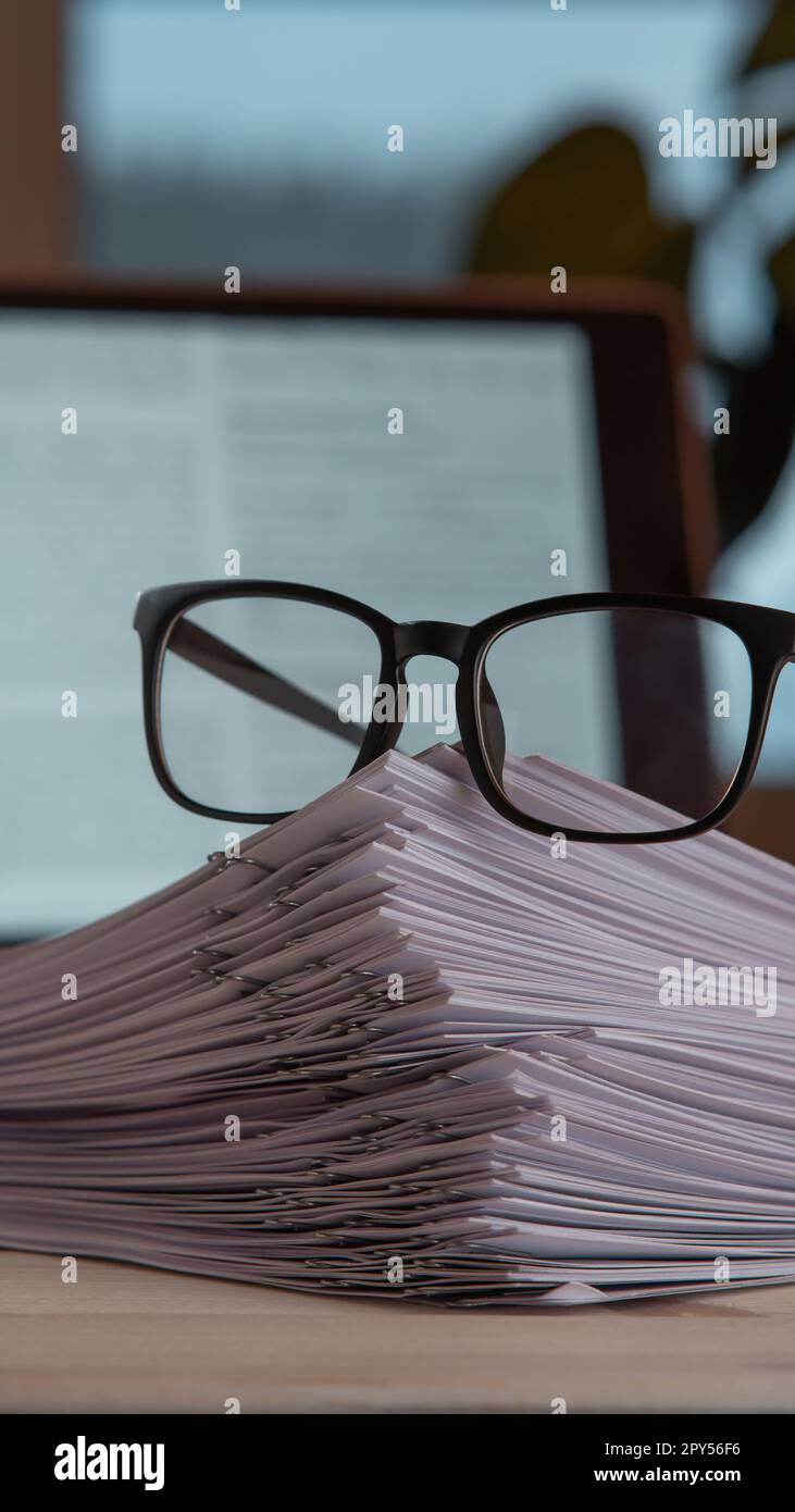 Zusammenstellung von Papierstapeln mit Büroklammern, Brille in der Nähe des Laptops auf dem Schreibtisch. Arbeitsbereich, Unternehmen, Technologie, Dokument. Stockfoto