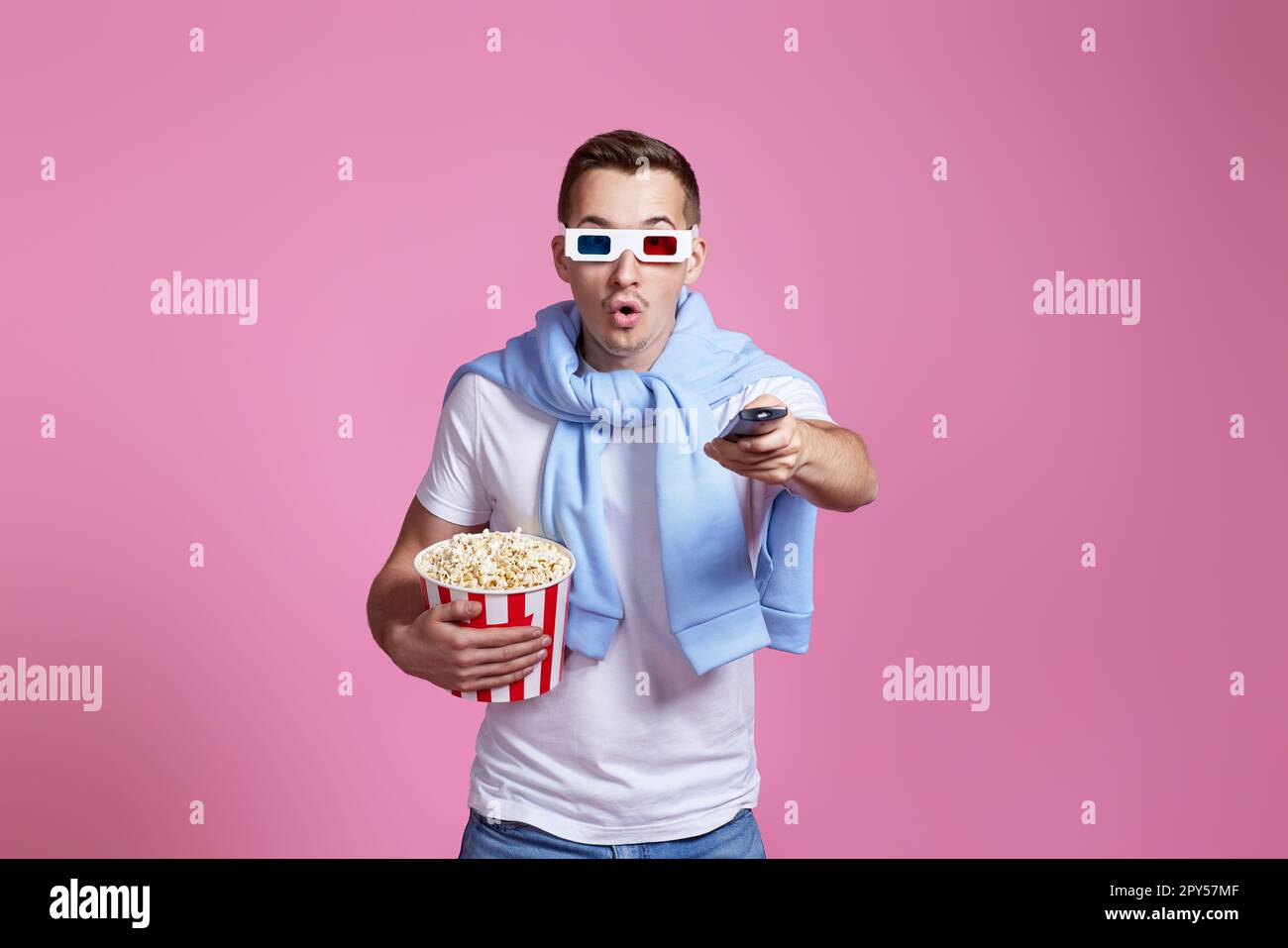 Ein Mann mit Fernbedienung, der sich einen Film mit einem großen Eimer Popcorn ansieht Stockfoto