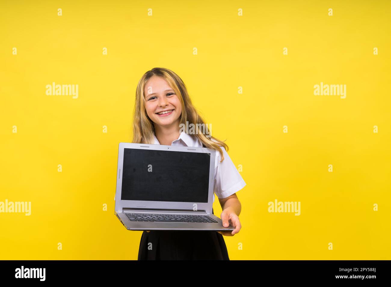 Ein kleines, glückliches, blondes Mädchen, das 12-13 Jahre alt ist, mit einem Laptop-pc. Kinderkinderkindliches Lifestyle-Konzept. Stockfoto