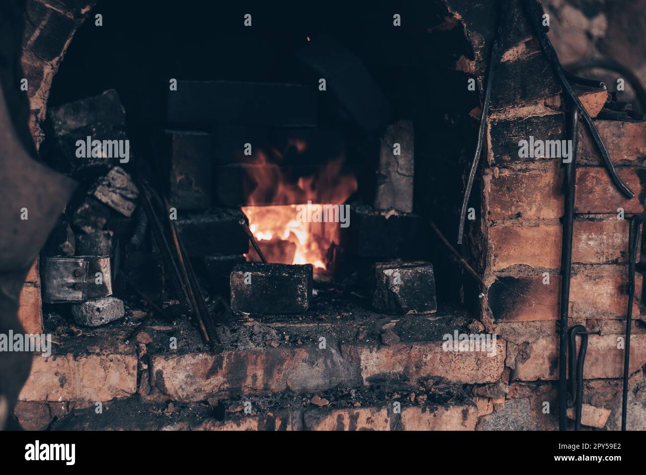 Alter Ziegelofen mit brennender Flamme in Schmiede. Herstellung von Eisen im Rußkamin in der Werkstatt. Metallarbeiten, Schmieden. Stockfoto