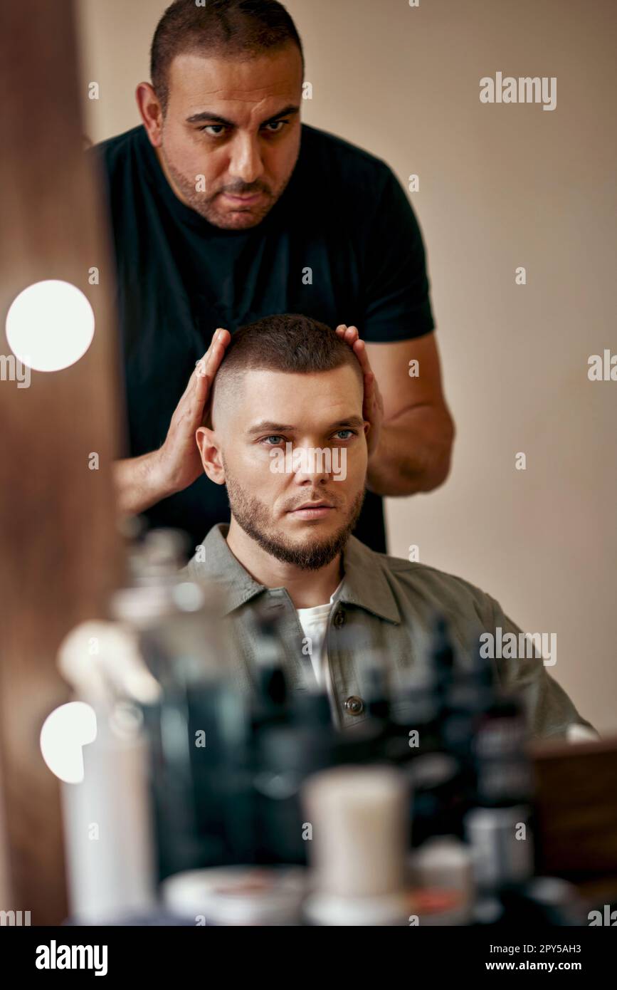 Friseur und zufriedener bärtiger Mann vor dem Spiegel Stockfoto