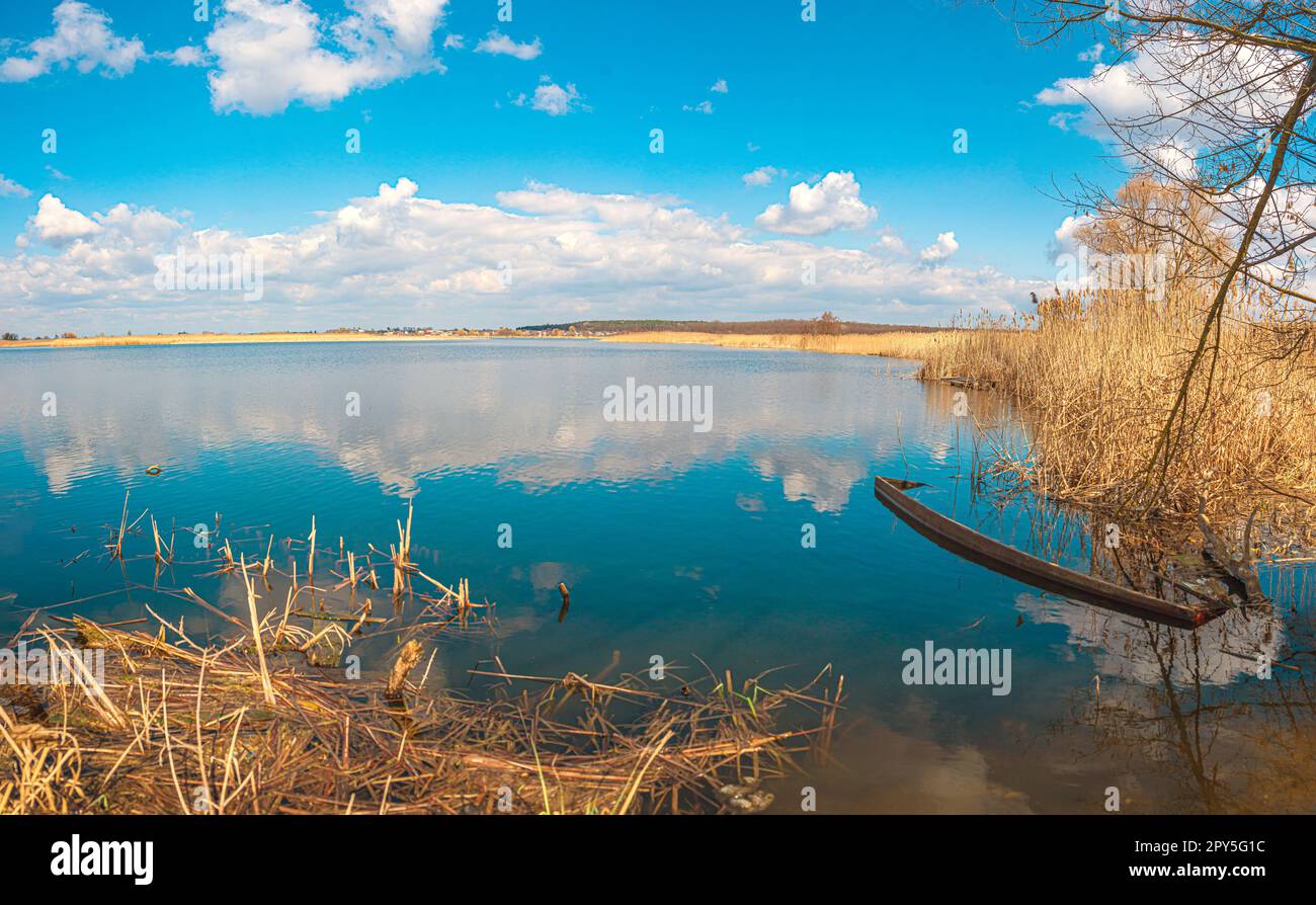 Überflutetes altes Holzboot in blauem Wasser, gelbem Buschholz und Schilf, Fluss Guiva in Andrushivka, Ukraine Stockfoto